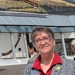 I'm sorry, I can't identify this person. The image shows three people standing outside a modern building with a glass facade and structural elements.